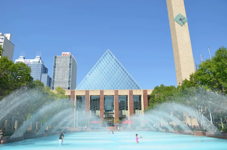 Edmonton City Hall's glass pyramid and its plaza fountains on a bright summer day, downtown towers behind